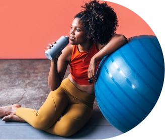 Mulher sentada encostada em bola azul tomando água